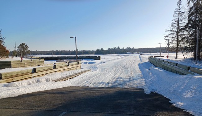 A ramp leads from the paved parking lot to the frozen lake, where a road has been plowed for vehicles.