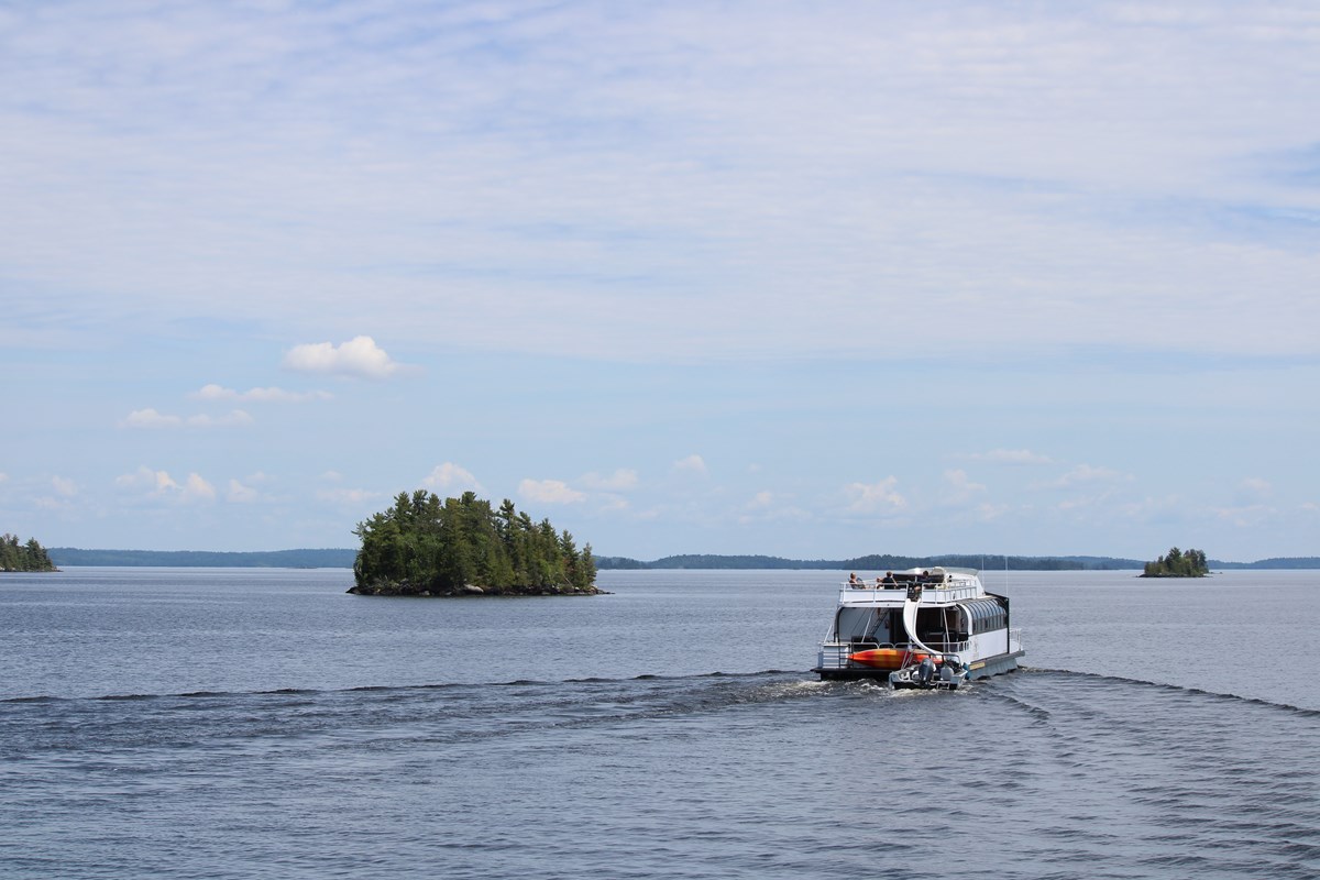 A houseboat boating on a large lake with small islands off in the distance.