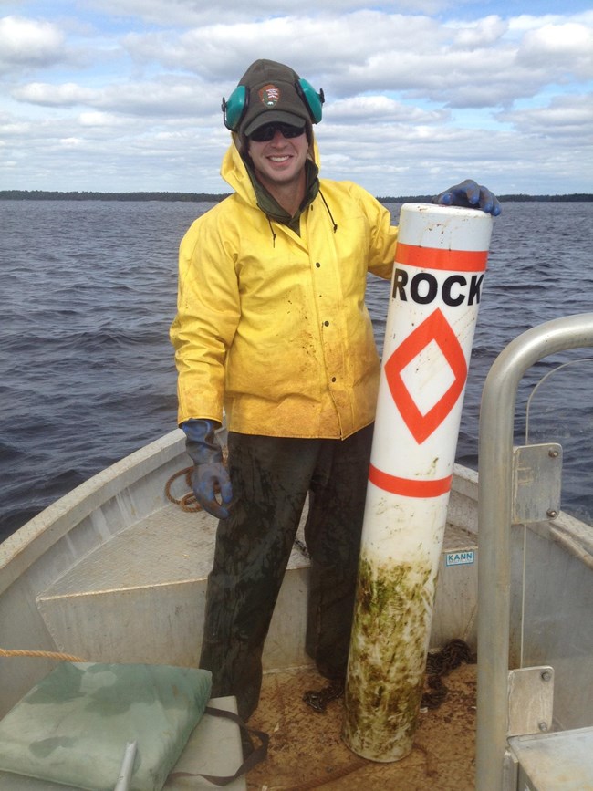 Park staff hold a rock hazard buoy while wearing a yellow rain jacket and standing in the front of a boat