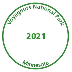A green circle marking the outter edges of a stamp. Within the green circle reads "Voyageurs National Park" and then "Minnesota" on the bottom and in the middle "2021" all in green text.