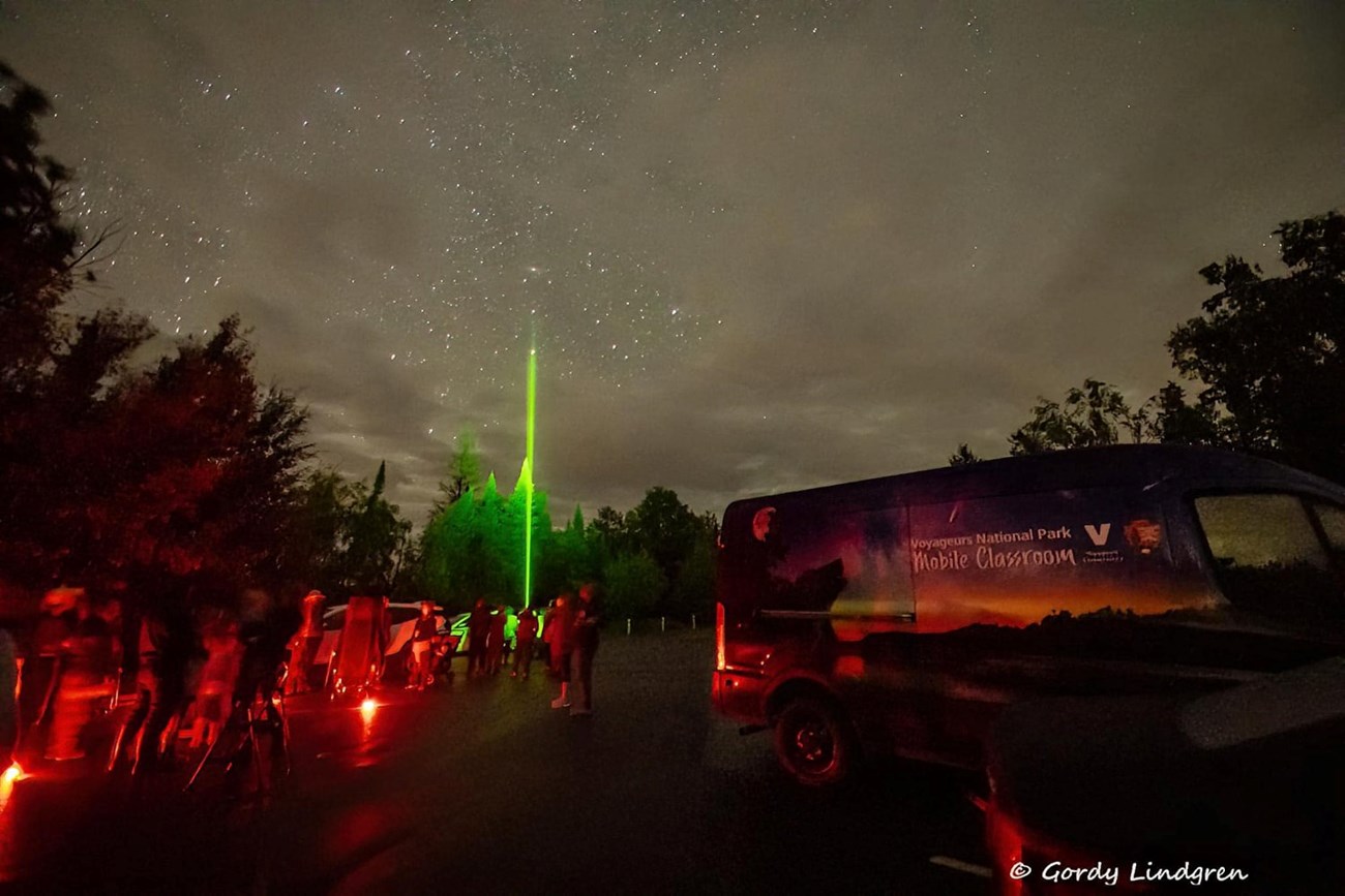A Park Ranger points a laser and visitors gaze up at the star-filled night sky.