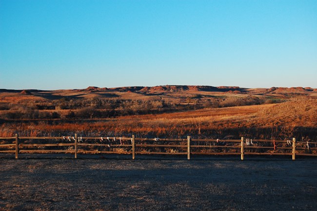 Washita Battlefield with fence in foreground and hills and ridges in background at sunset