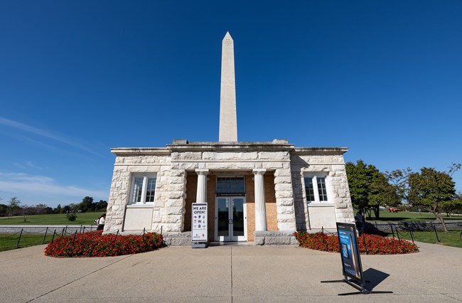 The double door entrance to the Washington Monument Lodge. Two signs sit near the entrance. The Washington Monument peeks up through the back of the Lodge.