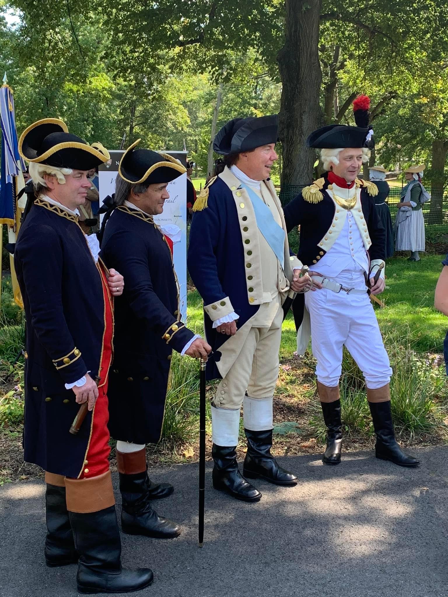 Four living historians dressed in 18th-century military uniforms—portraying French and American officers from the Revolutionary War era—stand together outdoors during a public event, smiling and posing for visitors.