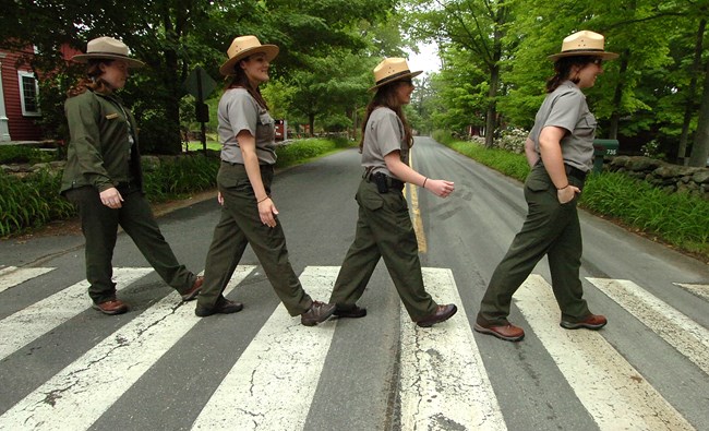 Four park rangers pose in profile crossing a road at a crosswalk, mimicking the Beatles' Abbey Road album cover.
