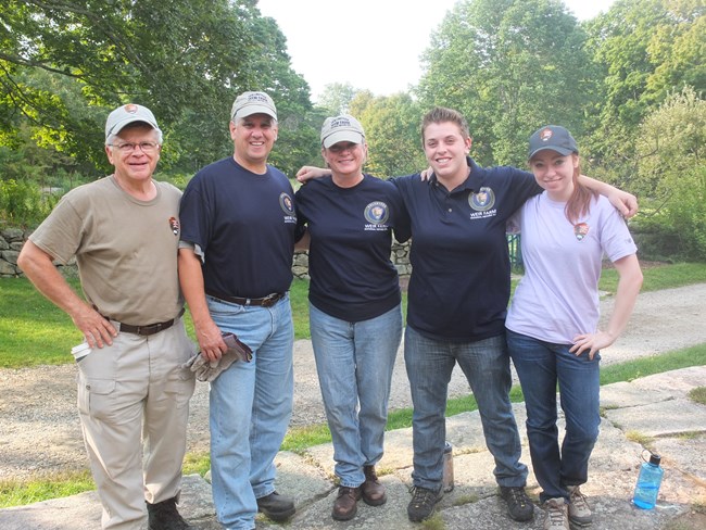 A group of five people wearing volunteer uniforms smile with their arms around each other.
