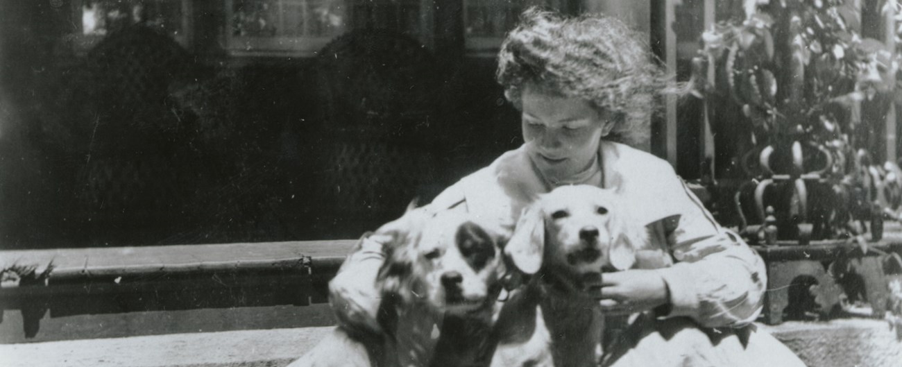A black and white photo of a young women holding two dogs in her arms.