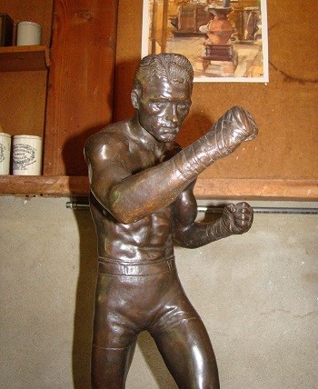 A bronze statue of a boxer with his hands raised and wrapped up with tape.