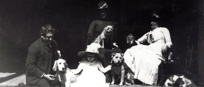 A black and white photo of a family and their dogs sitting on porch.