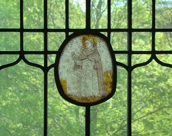 A stained glass window of a saint sitting the the grass.