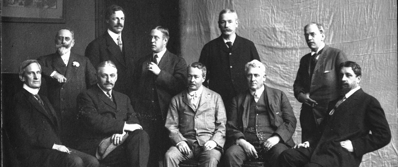 A black and white group photo of ten men, some standing while others sit.