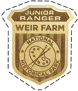 A wooden junior ranger cut badge with two paint brushes and a palette that says "Junior Ranger Weir Farm National Historical Park"