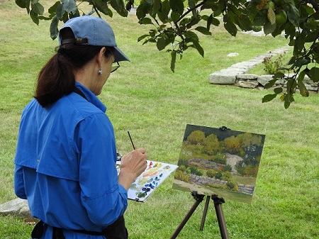 An artist standing next to an easel, painting a garden.