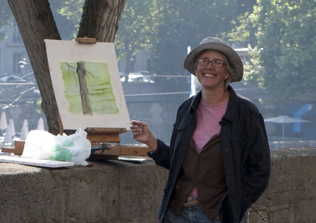 May Artist-in-Residence Amanda Parry Oglesbee A painter smiles in front of an easel outdoors.