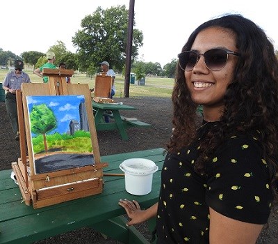 A young artist standing in front of her easel on a picnic table