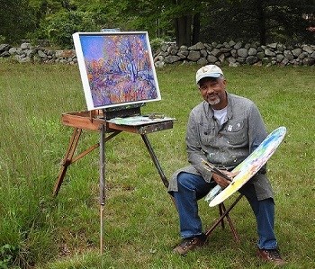 An artist sitting next to his easel in a field.