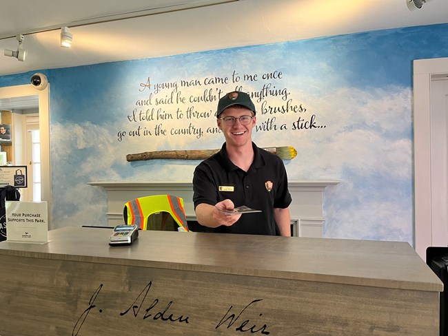 A smiling park ranger hands a brochure over a desk.