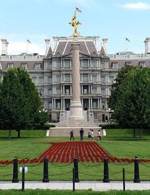 A marble column with a winged gold figure on top. A large, red number one is formed by flowers planted in front of the column.