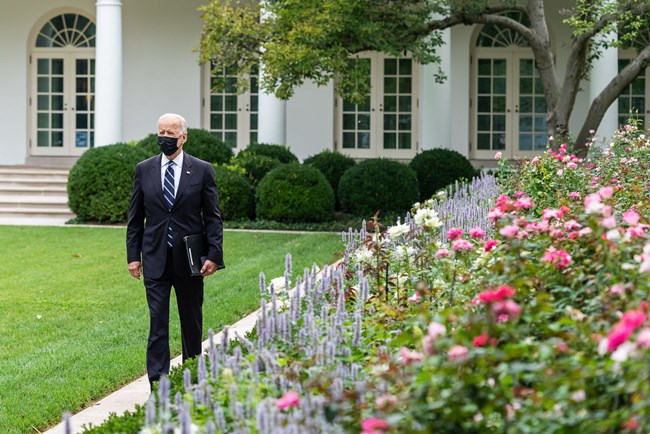 President Biden walks along a path with flowers outside the White House.