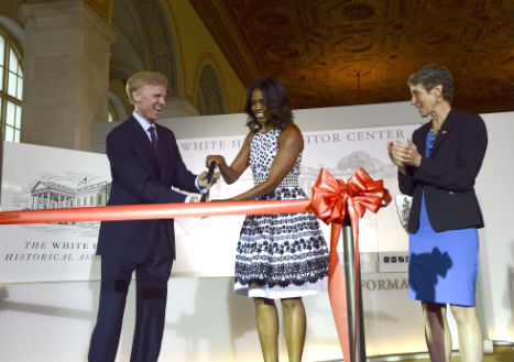 First Lady Michelle Obama cuts a large ribbon with an oversized pair of scissors, flanked by Secretary of Interior Sally Jewell and Chairman of the White House Historical Association Fred Ryan.