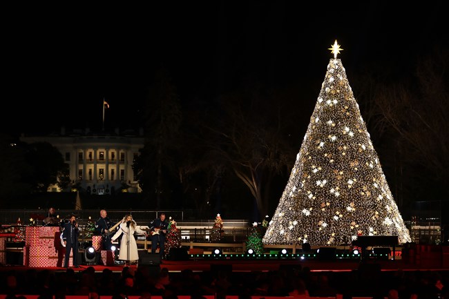 Jessie James Decker sings onstage flanked by a huge Christmas tree lit with white lights with the White House illuminated in the background.
