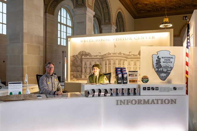 Two park rangers sit behind an information desk.