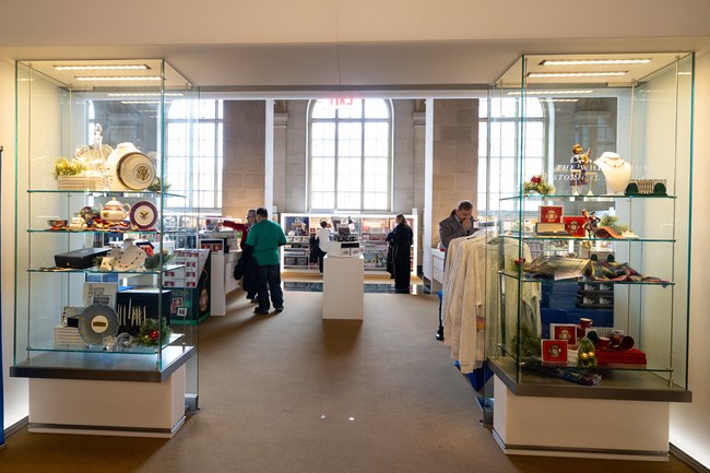 Two glass cases with souvenirs frame the entrance to a gift shop where visitors look at t-shirts, mugs, and other products.