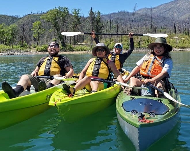 Four Latino park visitors in kayaks and smiling on Whiskeytown Lake on a sunny day.