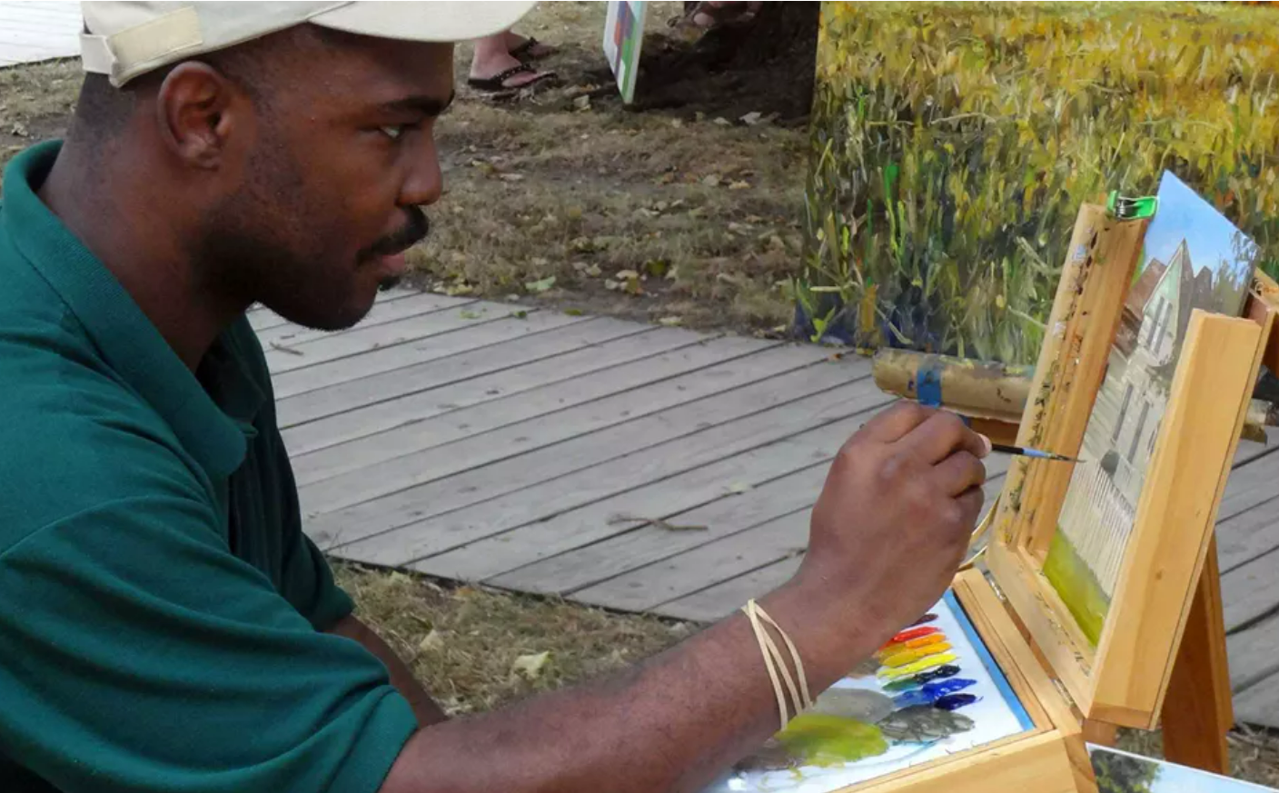 A black man in ball cap, painting.
