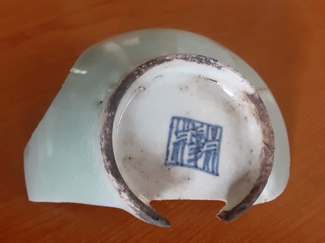 Light-colored Chinese pottery shard found in Whiskeytown. The Chinese characters are black and translate to "Lucky Great Mountain."