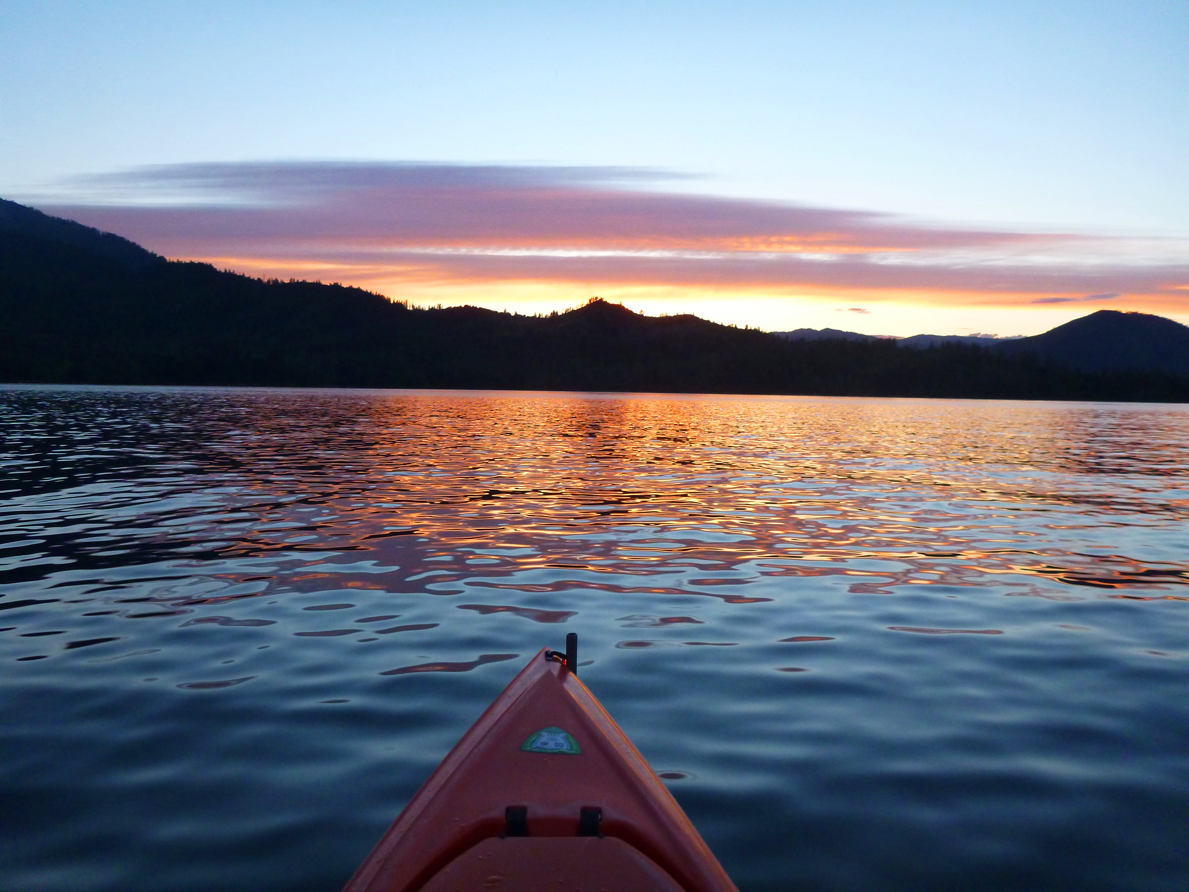 Tip of kayak on Whiskeytown Lake during sunset. Dark mountains and lake.