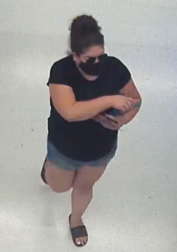photo of female suspect captured by camera surveillance. The suspect is wearing blue shorts, black t-shirt, sandals, glasses, a black facemask, and has dark hair.