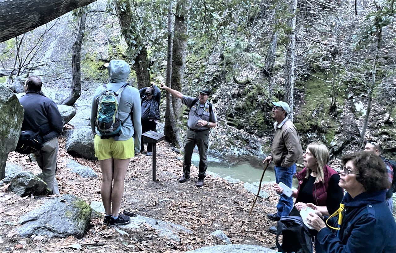 Ranger-led Hikes let you explore Whiskeytown while learning about the park's unique history. A groups of people on a ranger-led hike. An NPS ranger is pointing out some rock formations in a wooded environment.