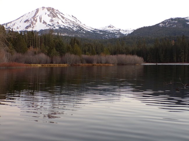 Lassen Park with snow on it, Manzanita Lake and shoreline in foreground.