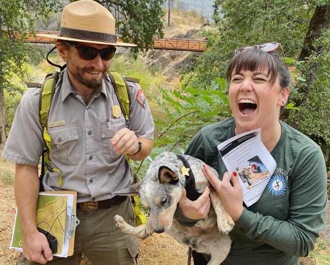 Park ranger, visitor, and dog laughing during ranger-led hike.