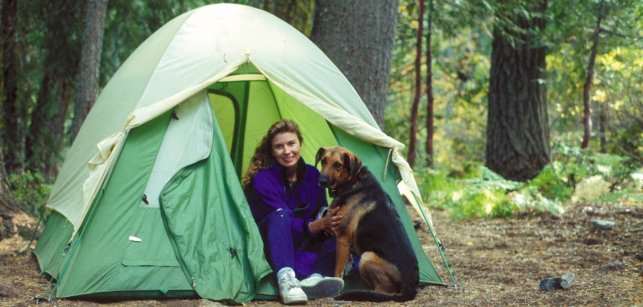 A visitor sitting outside of her green tent, with her dog next to her.