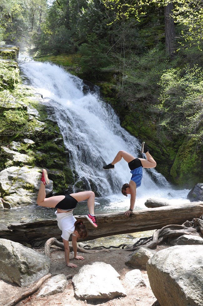 Two hikers making handstands and yoga poses at base of Whiskeytown Falls.