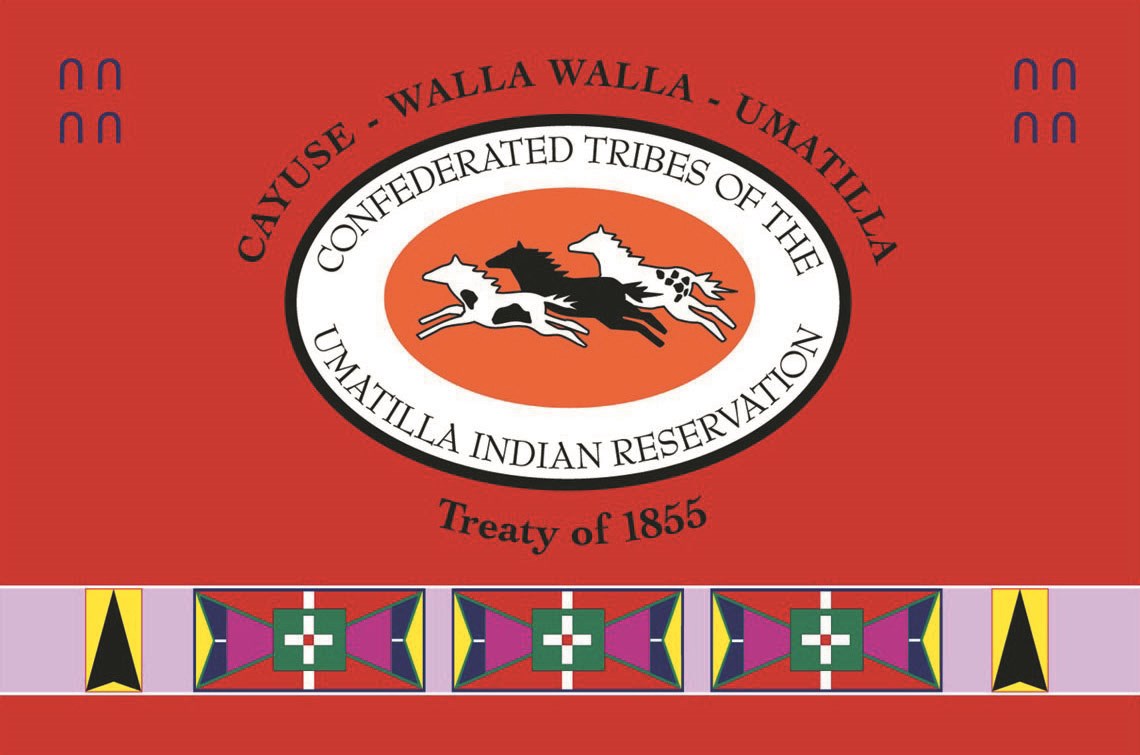 Confederate Tribes of Umatilla Indian Reservation Flag Three horses in an oval with text reading Confederated Tribes of Umatilla Indian Reservation. Text outside oval reads Cayuse - Walla Walla - Umatilla, Treaty of 1855. A band of geometric patterns runs along the bottom on a field of red.