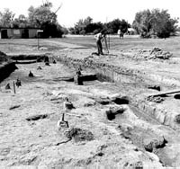 Archeological dig with man in distance making measurements.
