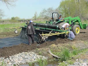 Large machine dispenses mulch cloth as it moves along.