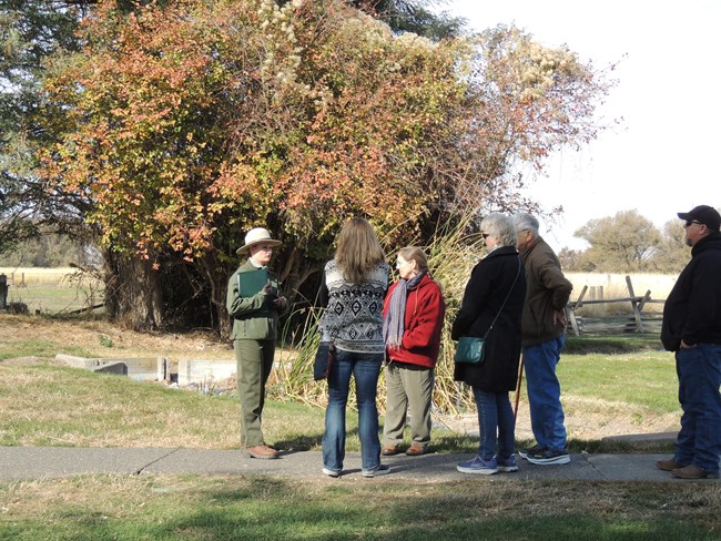 A ranger stands on a path in front of a group of visitors while speaking to the group