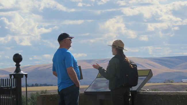 A visitor and ranger talk while at the top of a hill