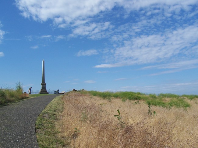 A hilltop with short green grass and a tall obelisk