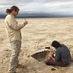 A man takes notes while another examines the ground
