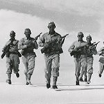 Army personnel marching on sand.