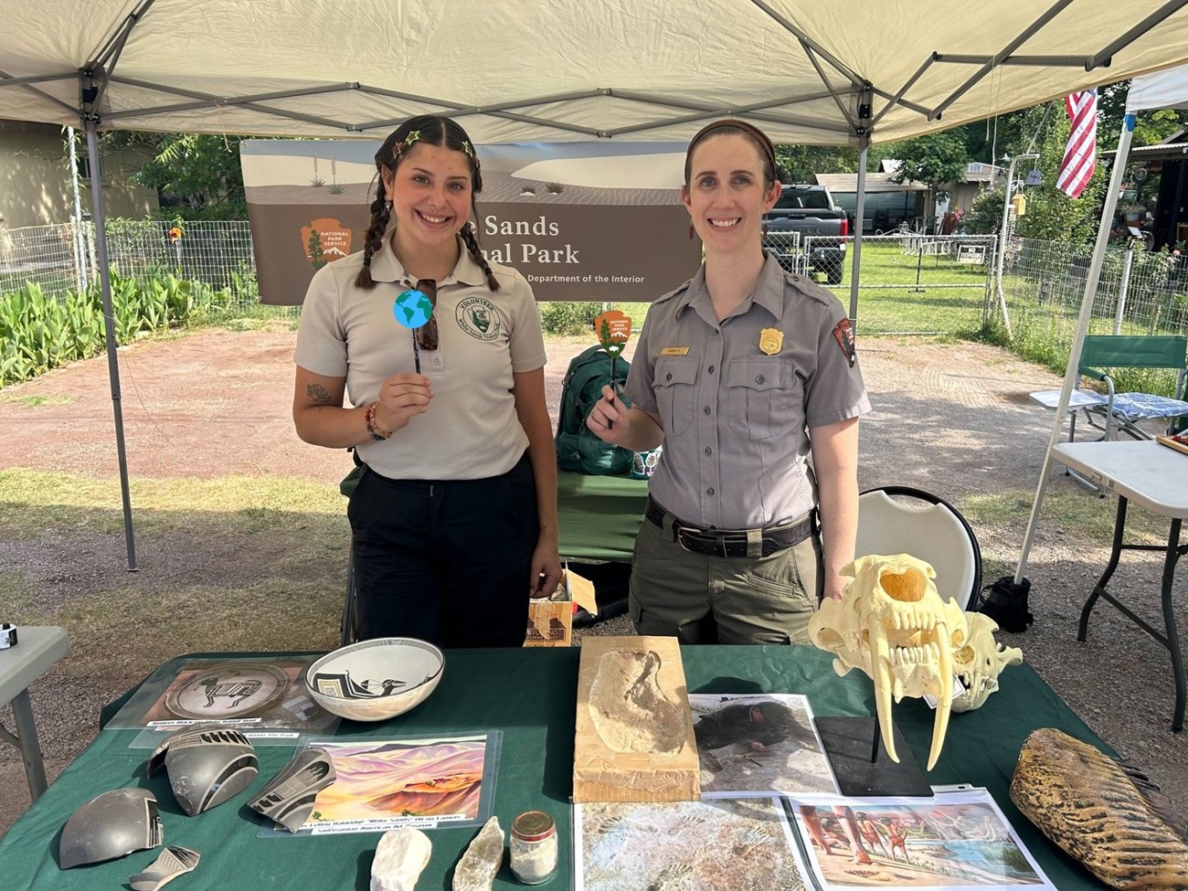 Two females, one volunteer and one ranger, stand smiling at a table with information about White Sands.