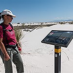 A woman looks at a trail sign in white sand dunes.