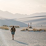 A hiker with a backpack heading toward a trail marker in white sand dunes.