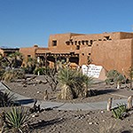 A brown adobe building with a graveled plant garden in front