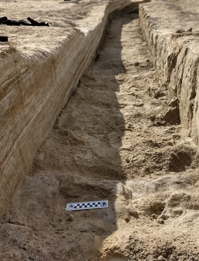 A trench dug into the brown gypsum soil on a lake playa in White Sands National Park.